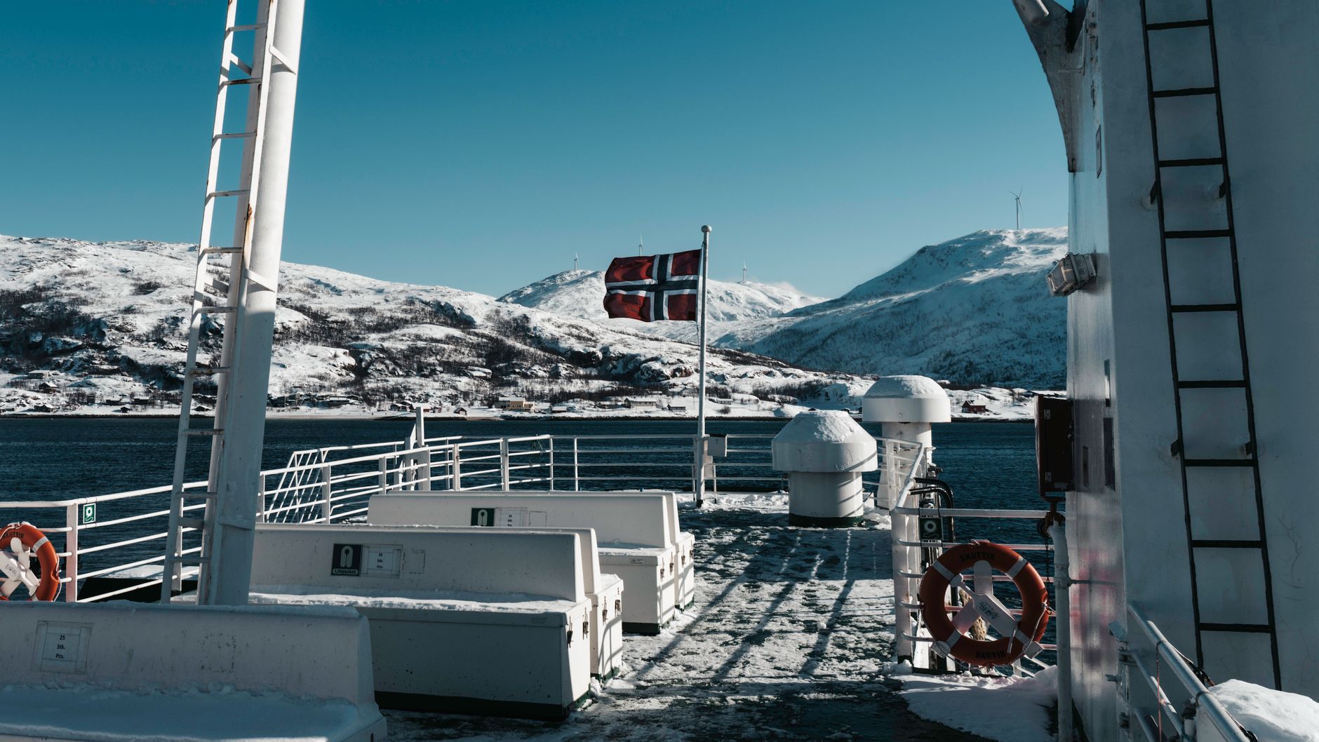 Pokład promu z flagą Norwegii na tle ośnieżonych gór zimą